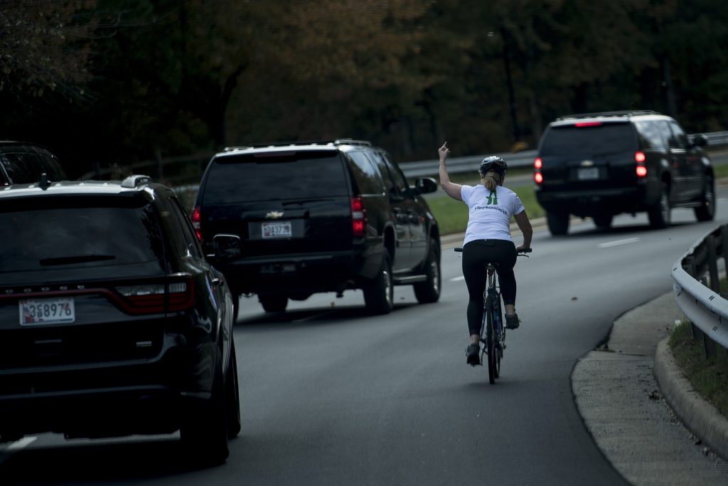 TOPSHOT - A woman on a bike gestures with her middle finger as a motorcade with US President Donald Trump departs Trump National Golf Course October 28, 2017 in Sterling, Virginia. / AFP PHOTO / Brendan Smialowski (Photo credit should read BRENDAN SMIALOWSKI/AFP/Getty Images)